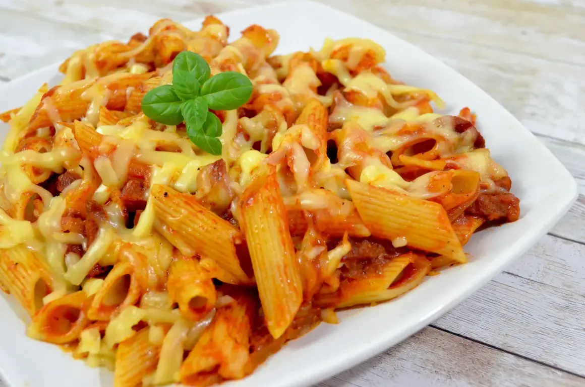 Penne z sosem pomidorowym i kawałkami pikantnego chorizo, zapieczone pod ciągnącym się serem. Udekorowane listkiem bazylii.