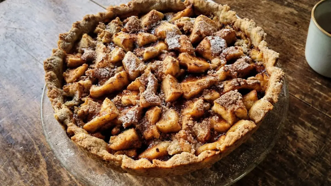 Apetyczna tarta na słodko z jabłkami i kruszonką, posypana cukrem pudrem. Idealna na deser.