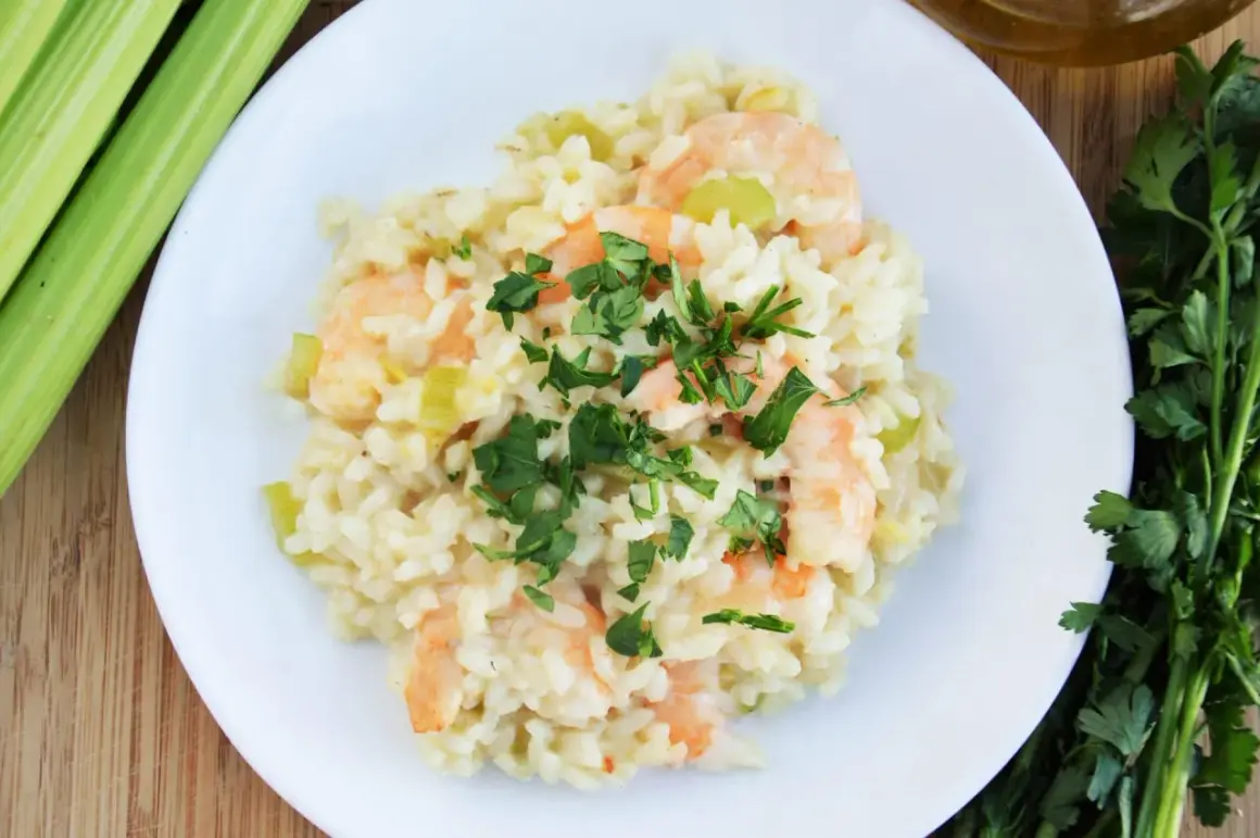 Pyszne risotto z krewetkami, ozdobione natką pietruszki, obok łodygi selera i butelka oliwy.