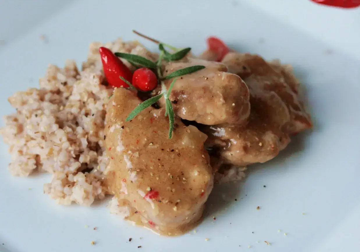 Miękkie polędwiczki wieprzowe w sosie, podane z kaszą, ozdobione chili i rozmarynem. Pyszne danie gotowe do spożycia.