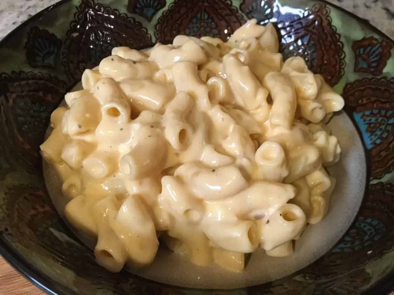 Porcja kremowego mac and cheese w ozdobnej misce. Makaron pokryty jest gęstym, serowym sosem z widocznymi kawałkami pieprzu.
