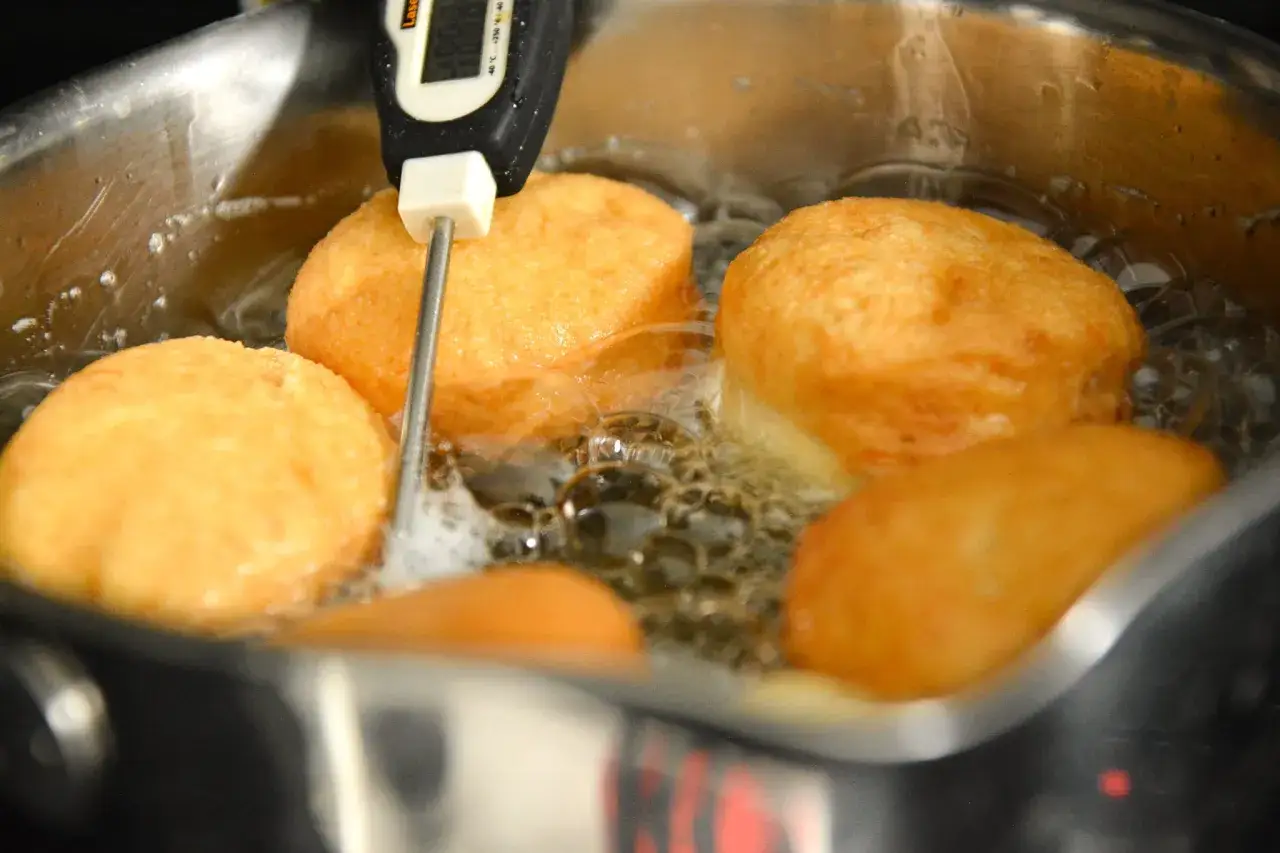 Pączki smażą się w głębokim tłuszczu. W garnku widać termometr kuchenny, który kontroluje temperaturę. Jaka mąka do pączków? Ta sprawi, że będą idealne!