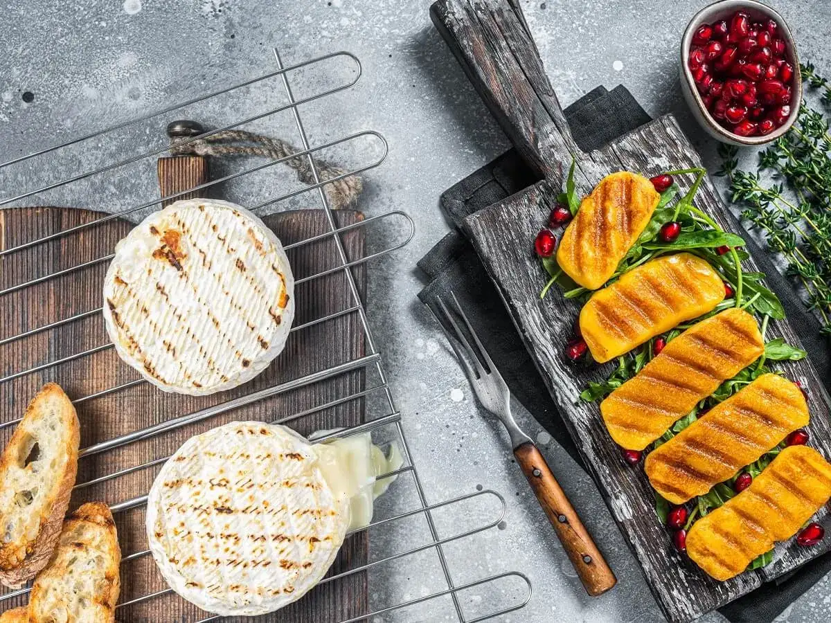 Dwa krążki serów na grilla, jeden lekko roztopiony, obok pieczywo i grillowane kawałki dyni z pestkami granatu.