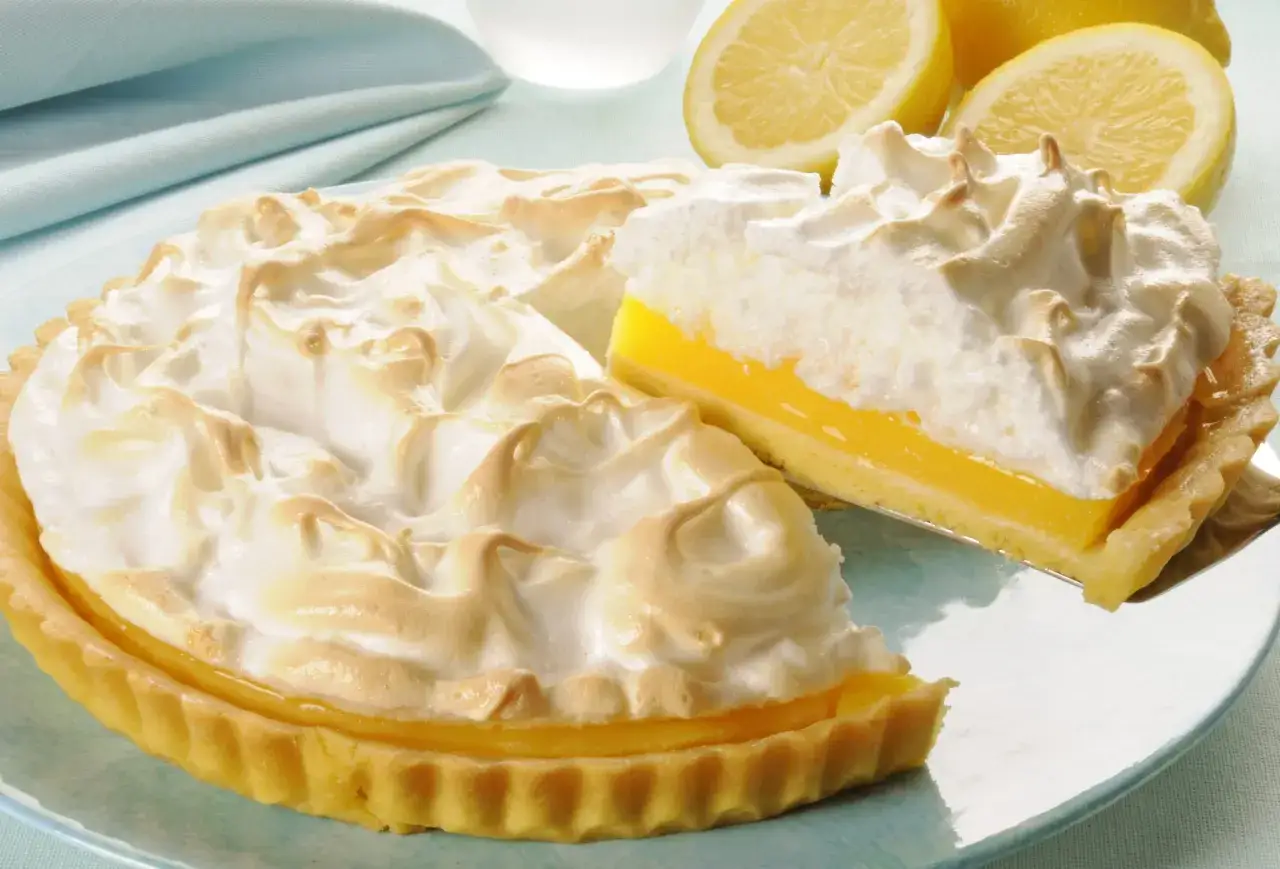 Puszysta tarta cytrynowa z bezą, z wyciętym kawałkiem, prezentuje się apetycznie na talerzu.
