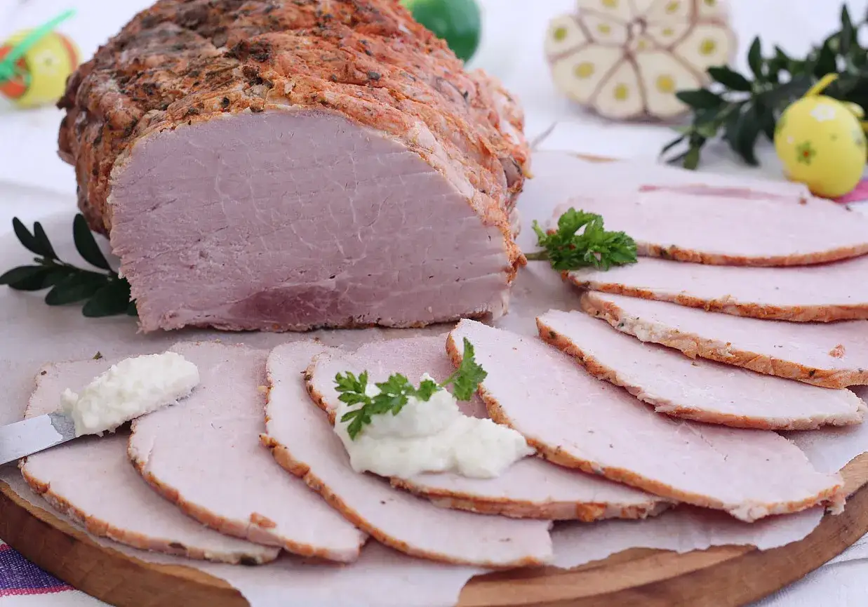 Soczysta szynka pieczona w rękawie, pokrojona w plastry, z chrzanem i natką pietruszki. Idealna na wielkanocny stół.