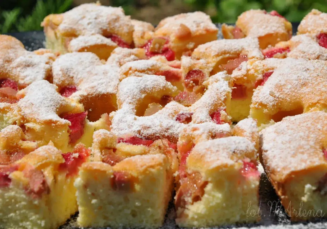 Pyszne ciasto z rabarbarem, pokrojone w kostkę i posypane cukrem pudrem, czeka na letnie popołudnie.