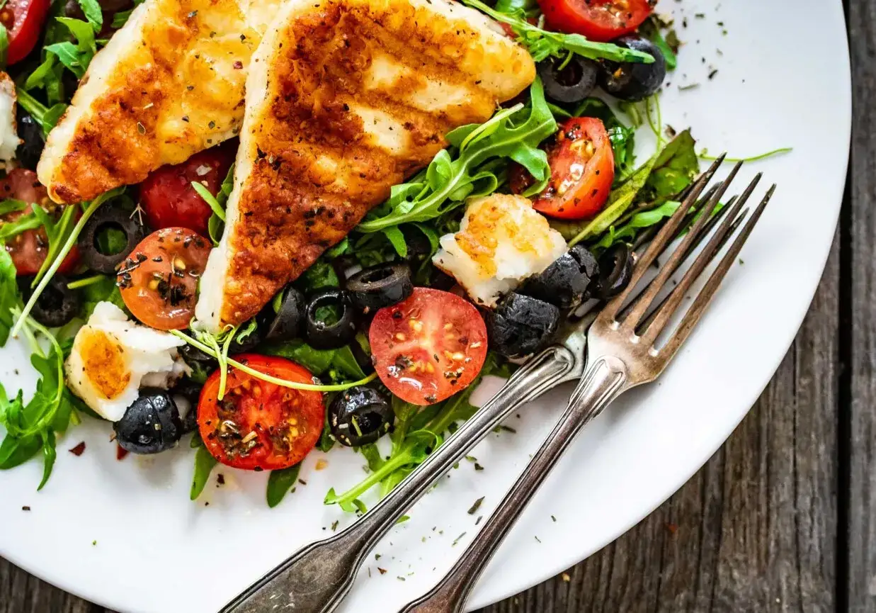 Pyszna sałatka z grillowanym halloumi, pomidorkami koktajlowymi i czarnymi oliwkami na talerzu.