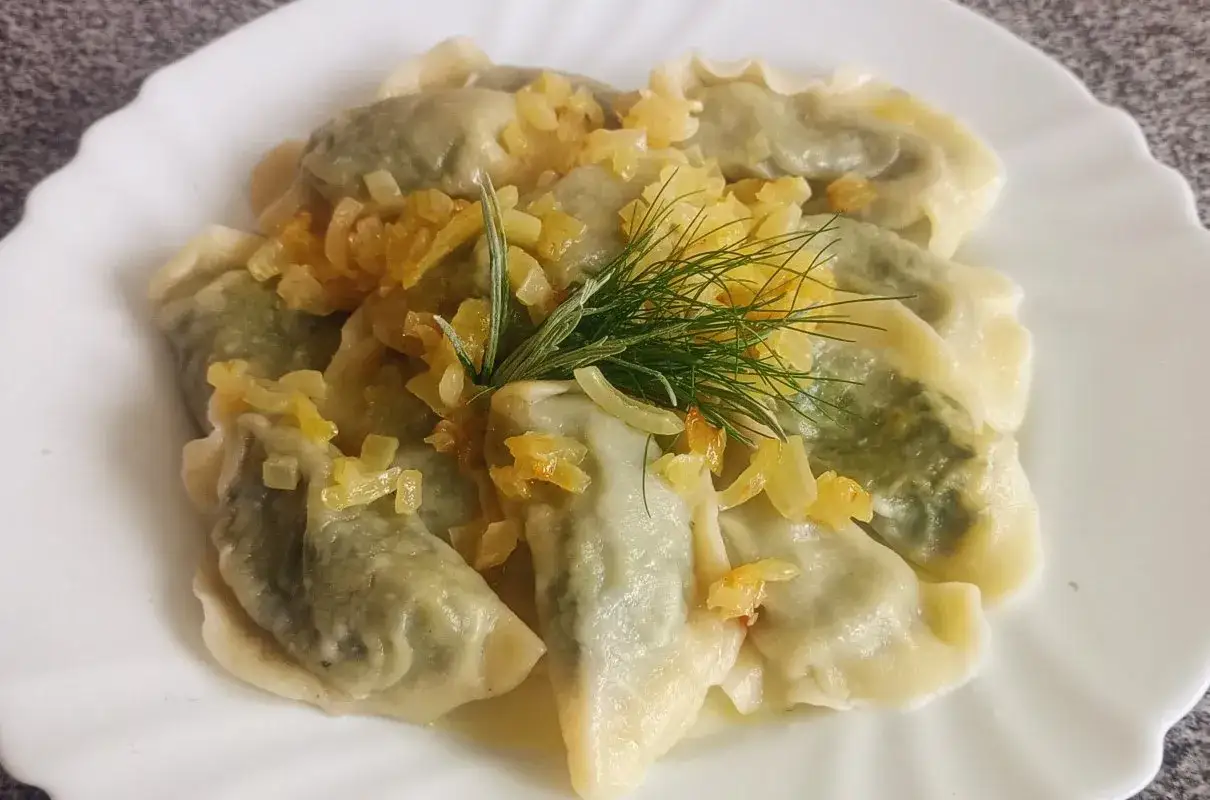 Pyszne pierogi ze szpinakiem, polane skwarkami z cebulki i udekorowane gałązką koperku. Idealne na obiad!