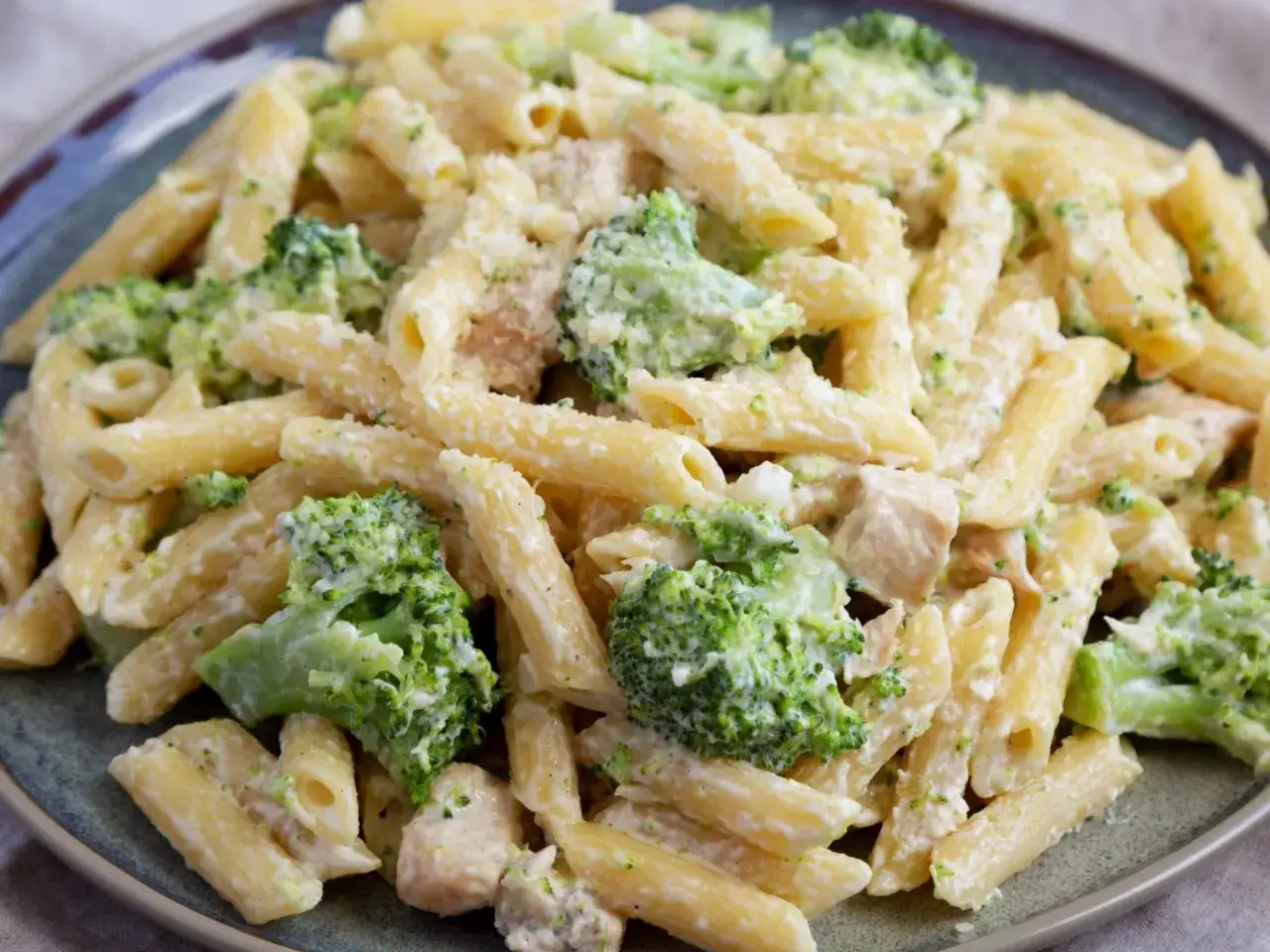 Penne z kurczakiem i kremowym sosem, obficie posypane zielonymi różyczkami brokułów. Pyszne makaron z brokułami na talerzu.