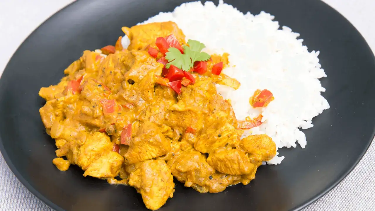 Pyszny kurczak w sosie curry z ryżem, udekorowany papryką i kolendrą. Idealny na szybki obiad.