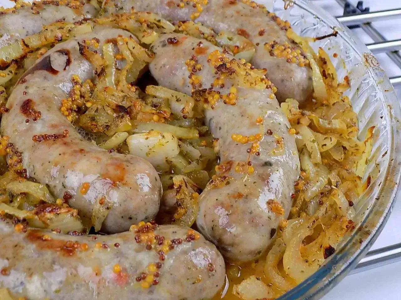 Pyszna biała kiełbasa pieczona w cebuli i musztardzie, z chrupiącymi ziarnami gorczycy. Idealna na obiad.