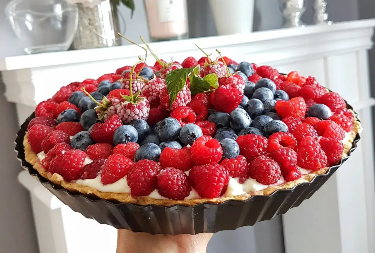 Pyszna tarta z truskawkami i borówkami, ozdobiona listkami mięty. Idealna na letnie popołudnie.