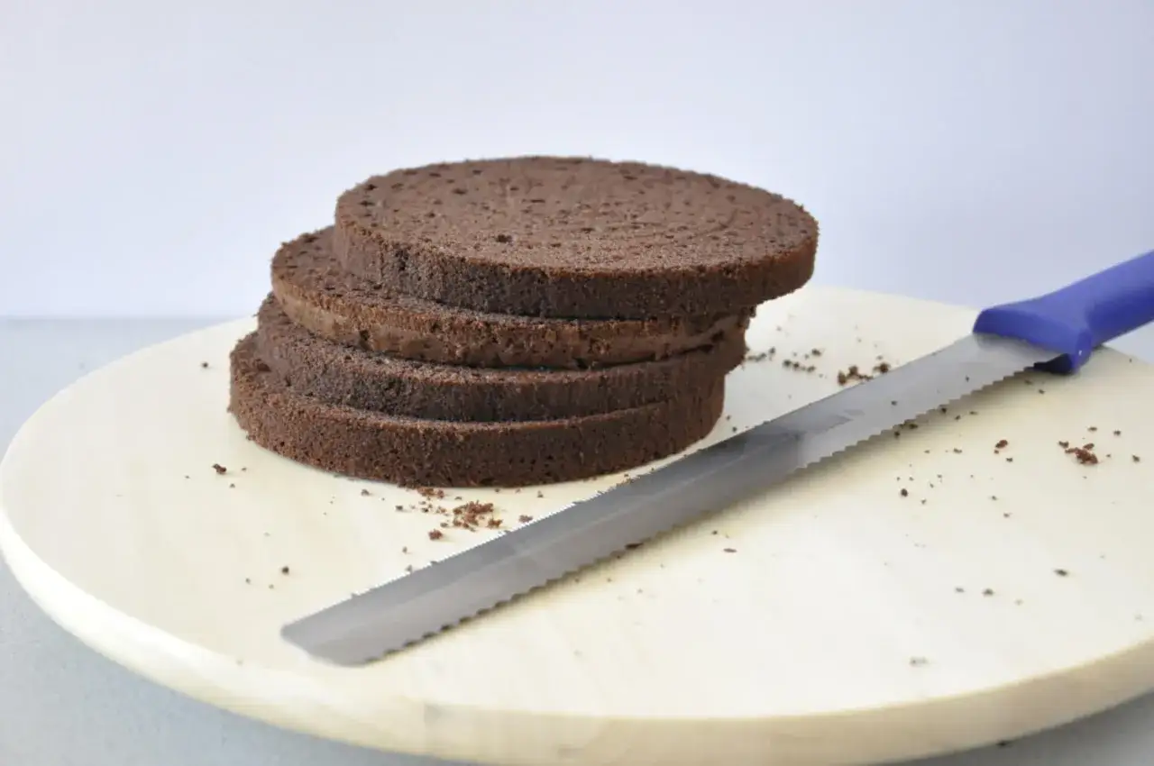 Stos ciemnych, puszystych krążków biszkoptu na tort, obok leży nóż do krojenia ciasta.