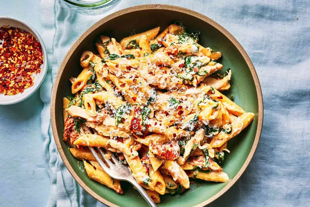 Pyszny makaron penne ze szpinakiem i suszonymi pomidorami w kremowym sosie, posypany parmezanem i płatkami chili.