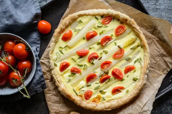 Pyszna tarta ze szparagami i pomidorkami koktajlowymi, udekorowana szczypiorkiem. Idealna na wiosenny obiad.