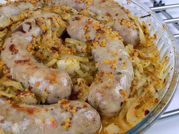Pyszna biała kiełbasa pieczona w cebuli i musztardzie, z chrupiącymi ziarnami gorczycy. Aromatyczne danie w szklanej formie.