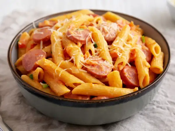 Penne z sosem pomidorowym i plasterkami kiełbasy, posypane parmezanem. Pyszny makaron z kiełbasą w misce.