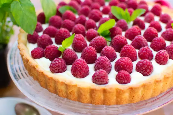 Pyszna tarta z malinami, udekorowana listkami mięty, kusi apetycznym wyglądem.