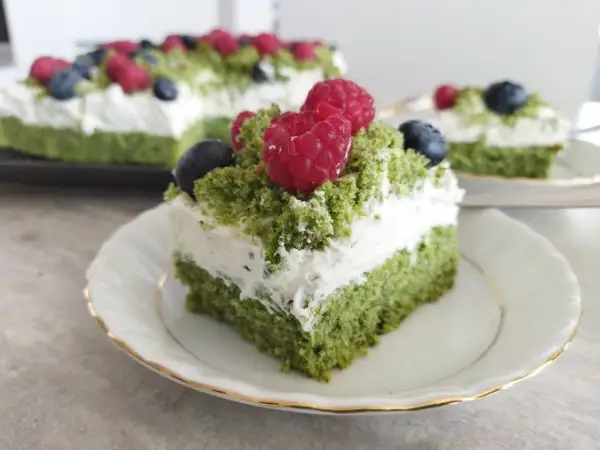 Zielony biszkopt przełożony kremem z mascarpone, ozdobiony malinami i borówkami. Pyszne ciasto leśny mech z mascarpone.