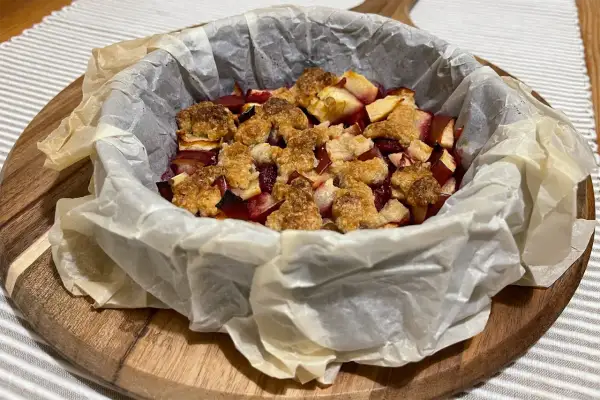 Pyszne owoce pod kruszonką, zapieczone w papierze do pieczenia, czekają na talerzu.