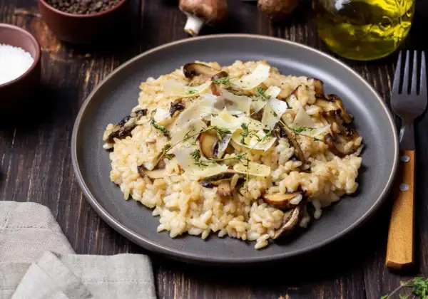 Aksamitne risotto z pieczarkami, posypane parmezanem i świeżym tymiankiem, prezentuje się apetycznie na ciemnym talerzu.