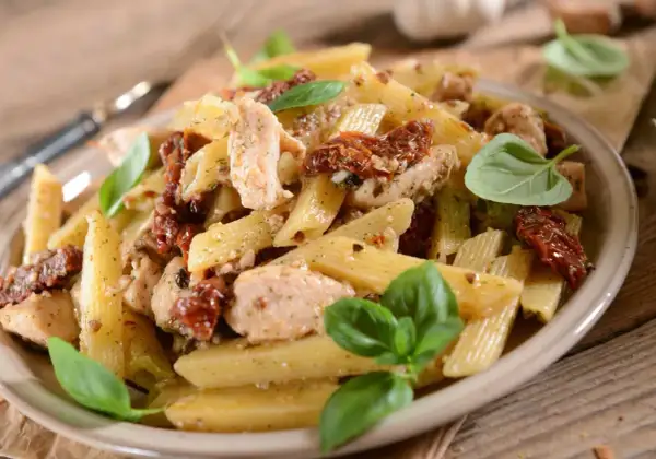 Penne z kurczakiem i suszonymi pomidorami, udekorowane świeżą bazylią. Pyszne danie, które zachwyci każdego smakosza.