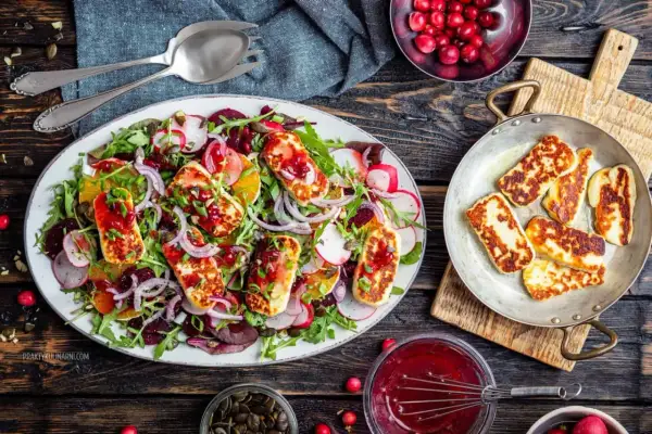 Kolorowa sałatka z grillowanym halloumi, burakami, pomarańczą i rukolą, polana sosem żurawinowym.