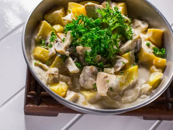 Pyszna potrawka z kurczaka z ziemniakami i pieczarkami w kremowym sosie, udekorowana natką pietruszki.