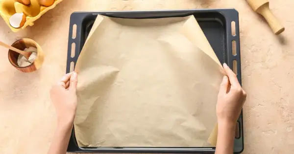 Dłonie układają papier do pieczenia na blasze. To świetne rozwiązanie, co zamiast papieru do pieczenia, gdy chcesz uniknąć przypalenia.