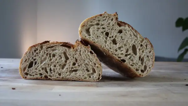 Chleb pszenno żytni na zakwasie, przekrojony na pół, prezentuje apetyczny, porowaty miąższ i chrupiącą skórkę.