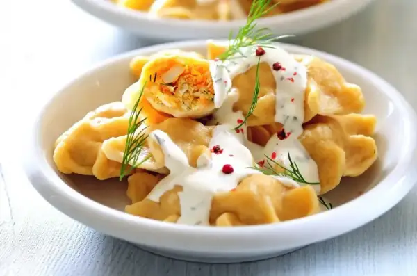 Elegancki obiad dla gości: pyszne pierogi z farszem, polane sosem śmietanowym, ozdobione koperkiem i różowym pieprzem.